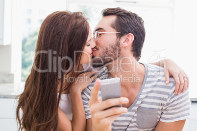 Young man using smartphone while girlfriend kisses him