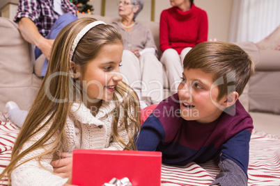 Smiling brother and sister lying and opening gift