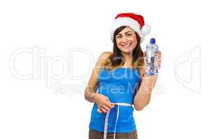 Festive fit brunette measuring her waist and holding bottle