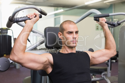 Serious young man working on fitness machine at gym