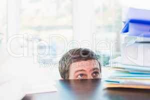 Scared businessman peeking over desk