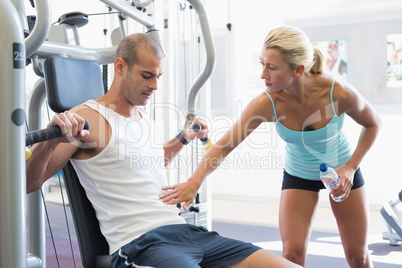 Trainer assisting man on fitness machine at gym