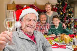 Smiling grandfather in santa hat toasting with champagne