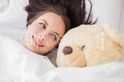 Pretty brunette under the duvet with teddy bear