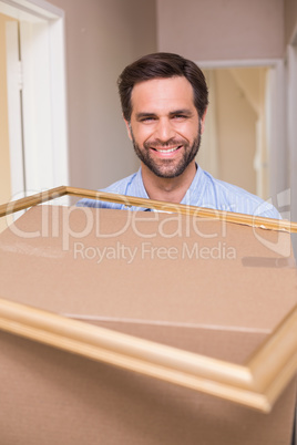 Happy man carrying moving box and frame