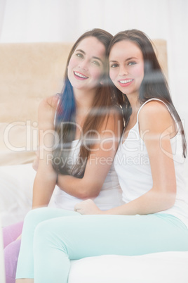 Pretty friends smiling at camera on bed