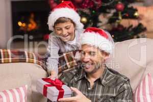 Son offering father a christmas gift on the couch