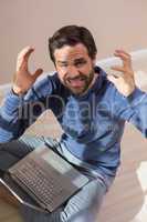 Strssed man sitting on floor using laptop