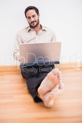 Relaxed businessman sitting on the floor while using laptop