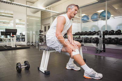 Injured man gripping his knee in the weights room