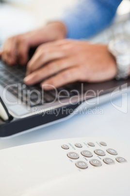 Hands of man typing on laptop near a phone