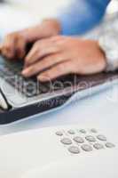 Hands of man typing on laptop near a phone
