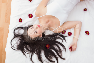 Pretty brunette posing in bed with flowers