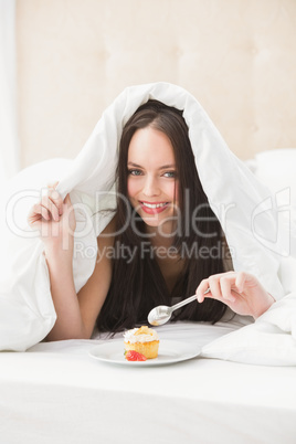 Pretty brunette eating cupcake in bed