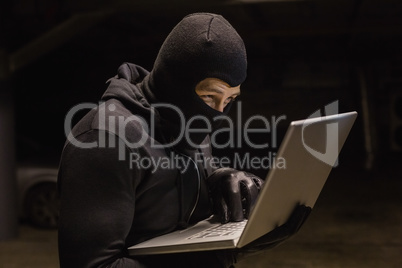 Focused burglar standing holding laptop
