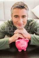 Smiling casual man resting head on piggy bank