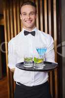 Cheerful young waiter holding tray with cocktails