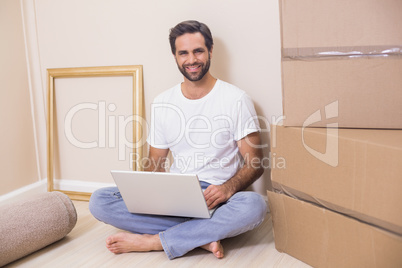 Happy man using laptop surrounded by boxes