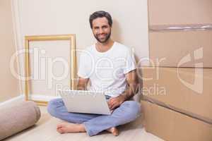 Happy man using laptop surrounded by boxes