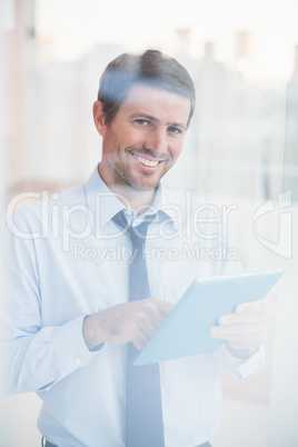 Smiling businessman using tablet looking out the window