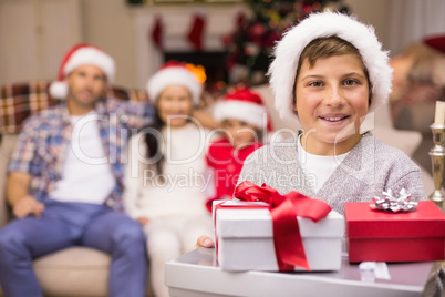 Festive son holding pile of gifts with his family behind