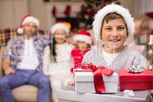 Festive son holding pile of gifts with his family behind