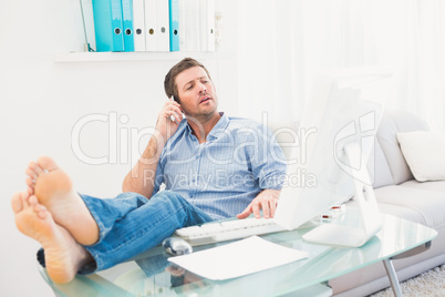 Businessman on the phone using his computer with his feet up