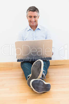 Happy man sitting on parquet using laptop
