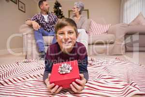 Happy son lying and holding gift with his family behind