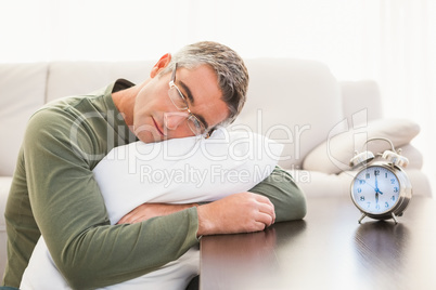 Man resting on cushion with alarm clock on the table