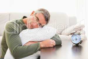 Man resting on cushion with alarm clock on the table