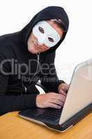 Hacker with white mask using laptop and looking at camera