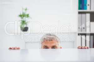 Nervous businessman peeking over desk