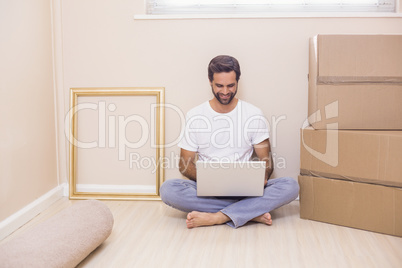 Happy man using laptop surrounded by boxes