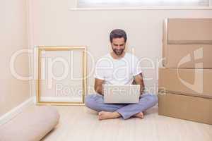 Happy man using laptop surrounded by boxes