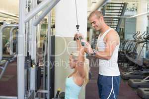 Trainer assisting young woman on a lat machine in gym