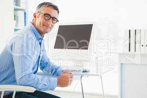Smiling man with glasses at his desk looking at camera