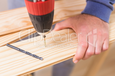 Casual man drilling hole in plank