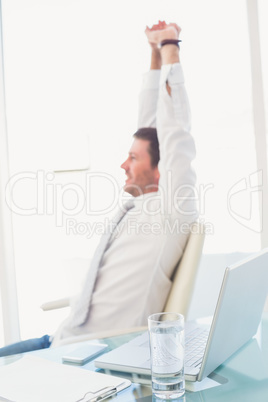 Smiling businessman stretching at desk