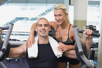 Trainer assisting man on fitness machine at gym