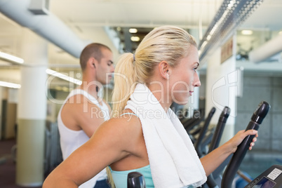 Side view of couple working on x-trainers at gym