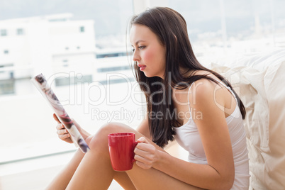 Pretty brunette sitting on floor reading magazine