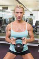 Serious woman lifting kettle bell in gym