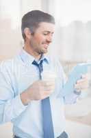 Smiling businessman using tablet holding disposable cup seen thr