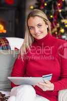 Festive blonde woman using her credit card and tablet pc