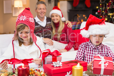 Festive little siblings opening a gift in front of their parents
