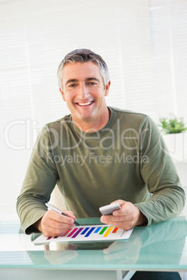 Smiling man analyzing chart and holding mobile phone