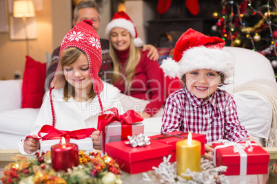 Festive little siblings opening a gift in front of their parents