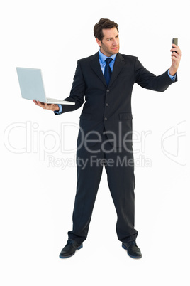 Businessman using laptop and texting on smartphone