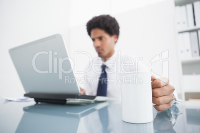 Businessman using laptop and holding mug at desk